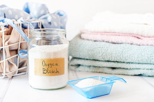 Photo with a small pile of laundry and a jar of oxygen bleach with scoop