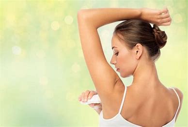 Image of woman with her back to us applying deodorant to her armpits